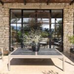 Outdoor patio with a stone wall, glass doors, a table with a potted plant, and seating on both sides.