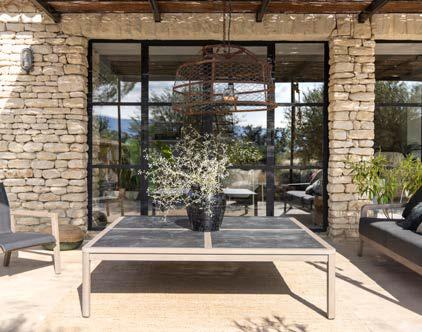Outdoor patio with a stone wall, glass doors, a table with a potted plant, and seating on both sides.