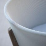 Close-up of a white fabric lampshade with a subtle texture, partially framed by a wooden support on a light background.