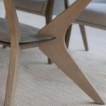 Close-up of wooden table legs with a modern, angular design on a light, textured carpet.