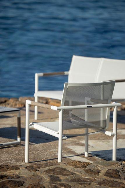 A white metal chair sits on a stone patio near the water, with another chair and a small table nearby.
