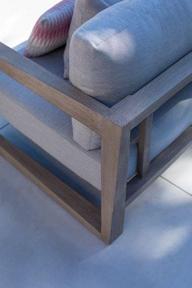 Close-up of a modern outdoor chair with light gray cushions, a wooden frame, and a patterned pillow on a tiled surface.