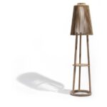 A modern wooden floor lamp with a slatted shade and tripod base, casting a shadow to the left on a white background.